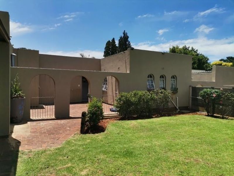 Rear view of the property featuring a brick-paved patio area with an arched colonnade, overlooking a well-maintained garden lawn.