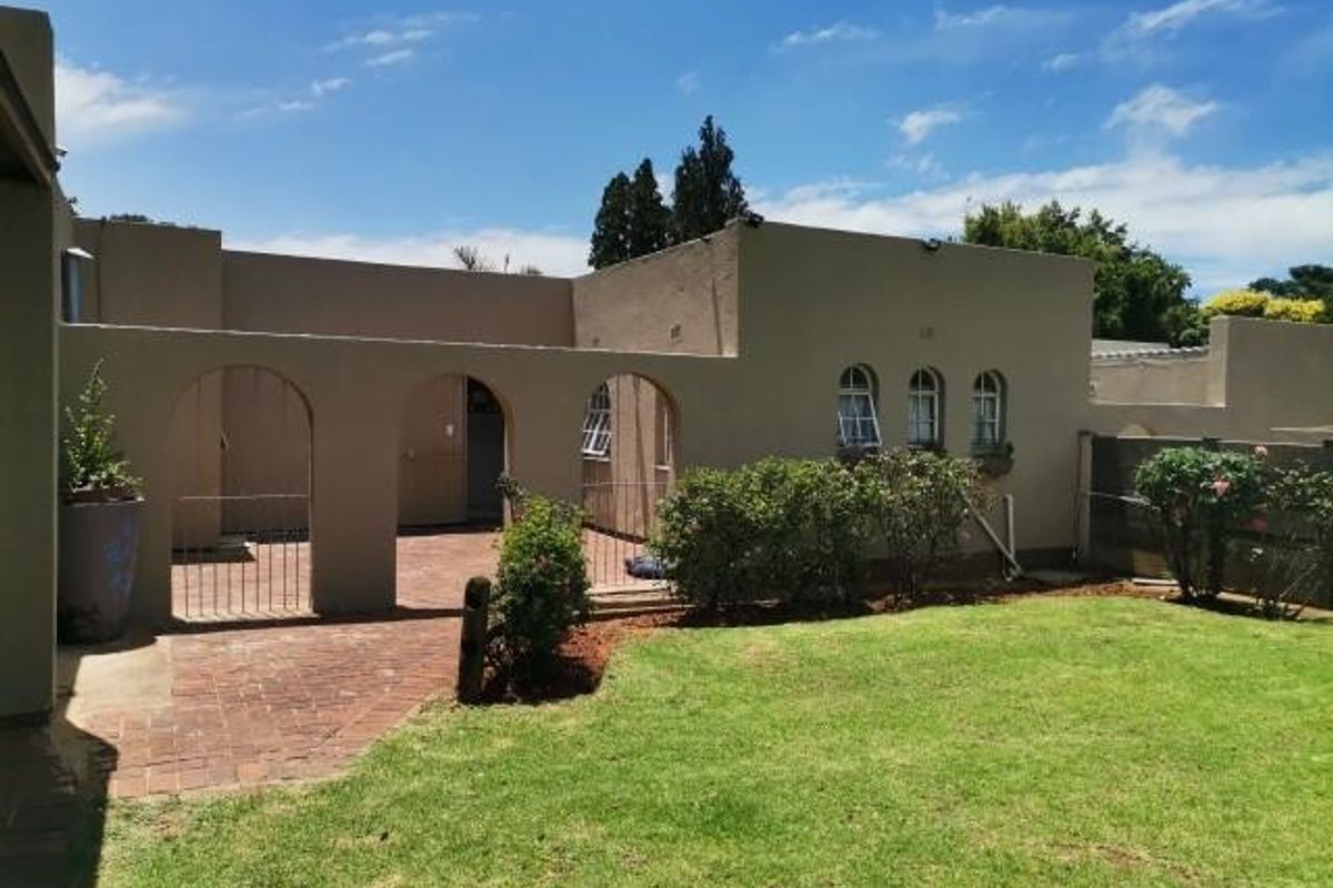 Rear view of the property featuring a brick-paved patio area with an arched colonnade, overlooking a well-maintained garden lawn.