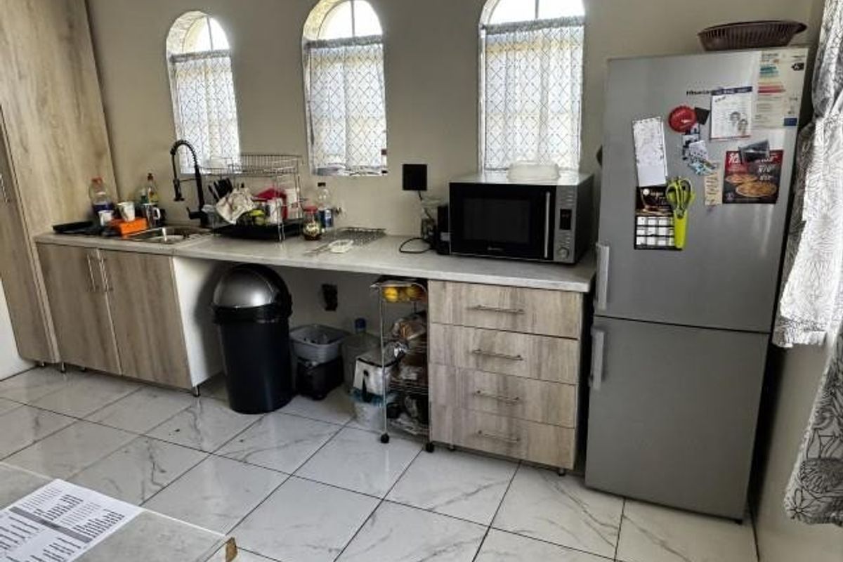 A functional kitchen featuring light wood-tone cabinetry, laminate countertops, tiled flooring, and distinctive arched windows providing natural light.