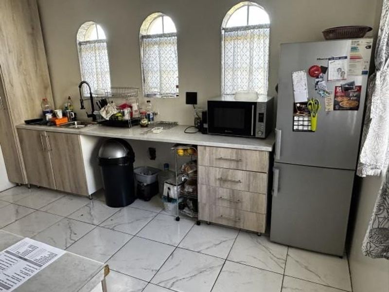 A functional kitchen featuring light wood-tone cabinetry, laminate countertops, tiled flooring, and distinctive arched windows providing natural light.