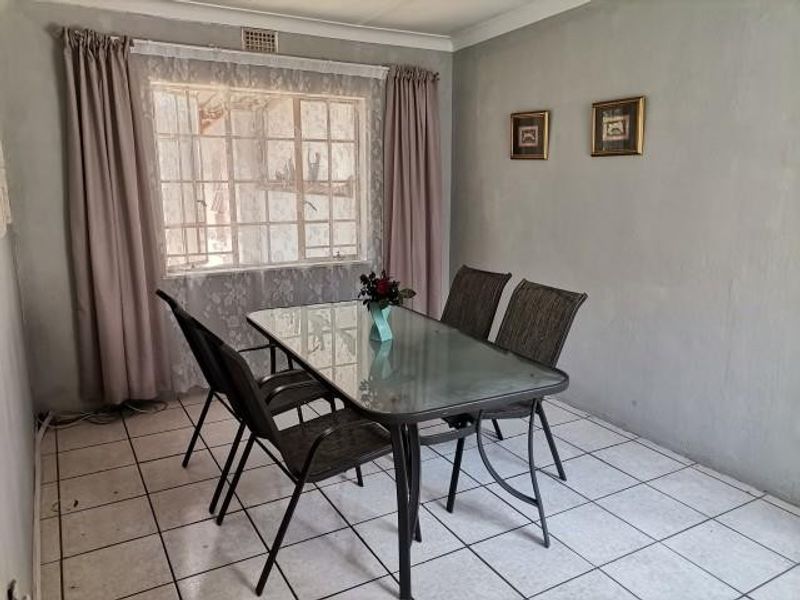 A dining area featuring tiled flooring and security burglar bars on the window, requiring cosmetic updates to improve the overall finish.