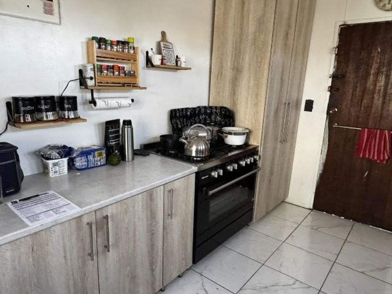 A functional kitchen featuring light wood-look cabinetry, laminate countertops, a gas stove with oven, and tiled flooring.