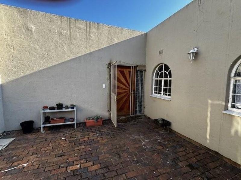 A rear courtyard area featuring brick paving, arched windows, and a security gate, showing signs of weathered exterior wall plaster.