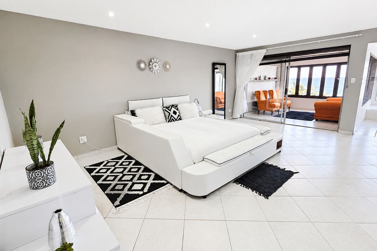 Spacious bedroom featuring tiled flooring, recessed lighting, and large sliding glass doors opening to an adjacent sunroom with ocean views.