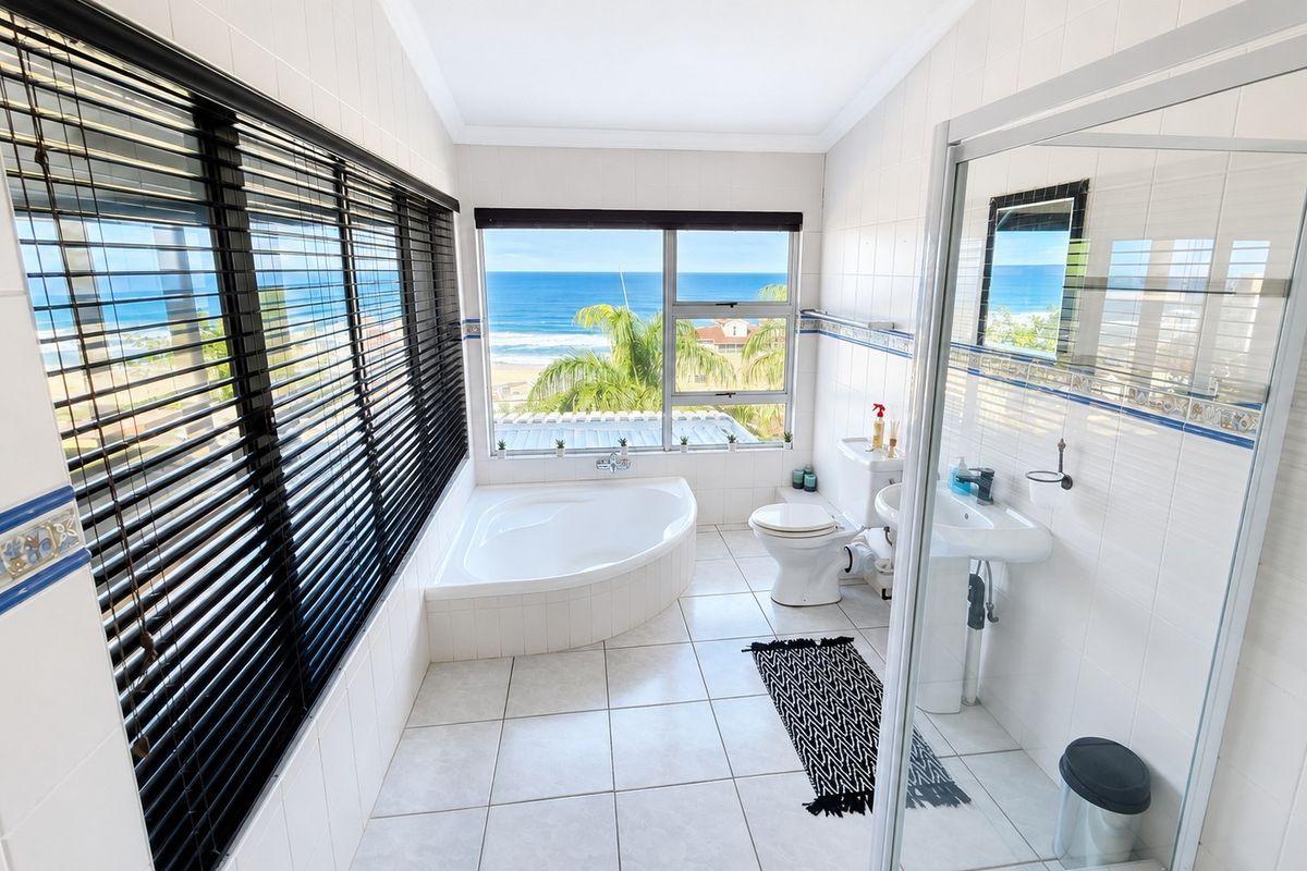 A bright bathroom featuring a corner bathtub, pedestal sink, and glass shower enclosure, offering expansive ocean views through large windows.
