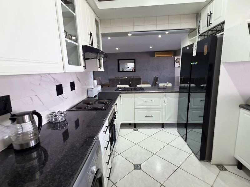 Modern kitchen featuring granite countertops, white cabinetry, marble-look backsplash, and integrated appliances, flowing into an adjacent dining area.
