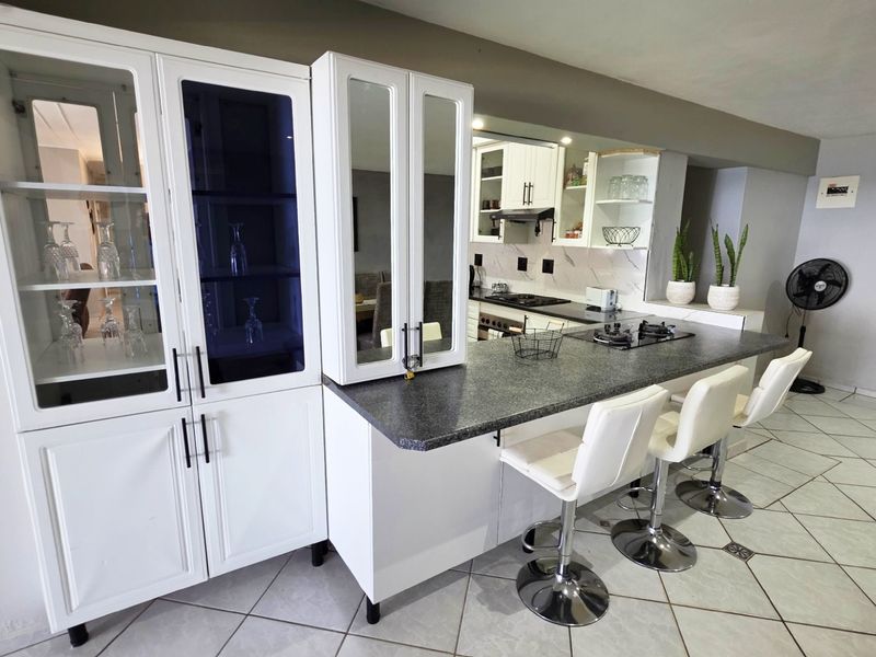 A well-maintained kitchen featuring white cabinetry, a stone breakfast bar with integrated gas hob, and tiled flooring in an open-plan layout.