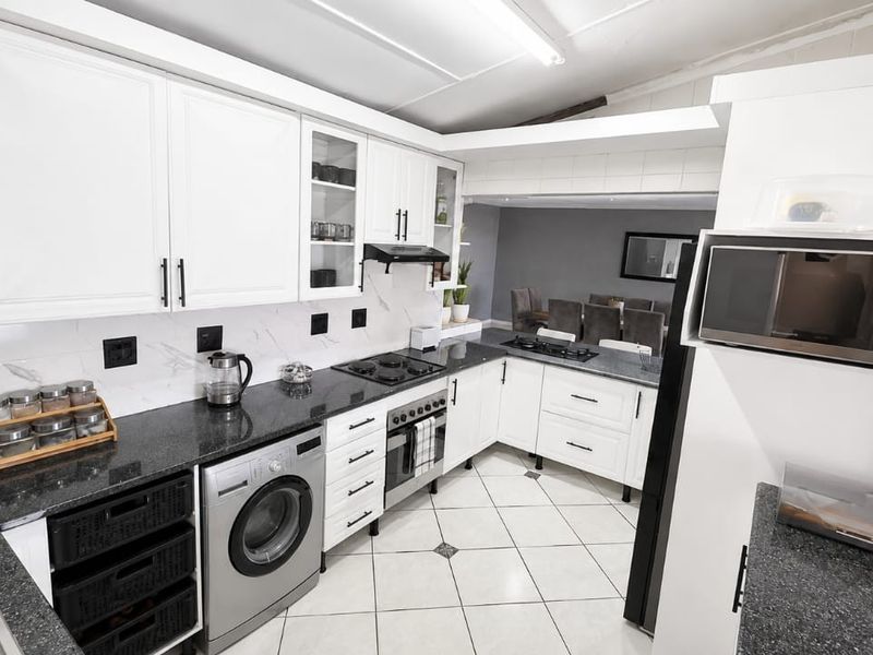A well-maintained kitchen featuring white cabinetry, dark granite countertops, a gas hob, built-in oven, and integrated microwave with tiled flooring.