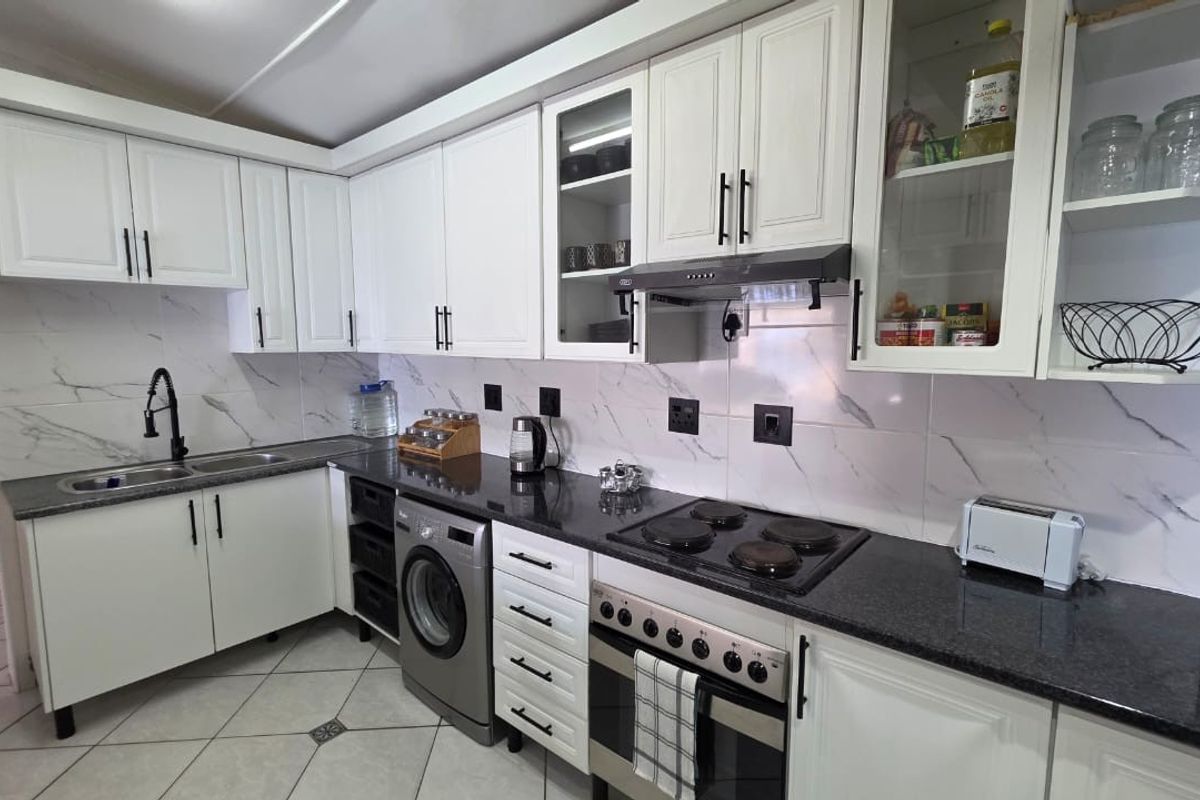 A well-maintained kitchen featuring white cabinetry, granite countertops, marble-look backsplash, and integrated appliances including an oven, hob, and extractor fan.