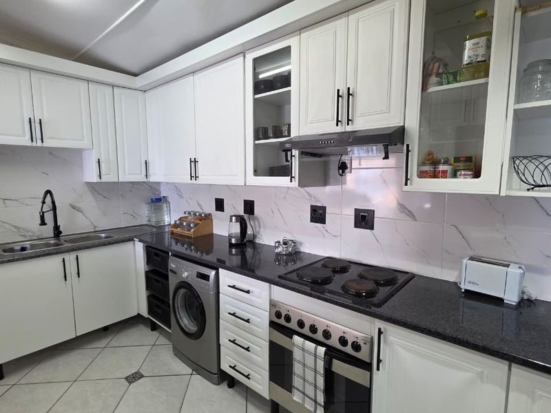 A well-maintained kitchen featuring white cabinetry, granite countertops, marble-look backsplash, and integrated appliances including an oven, hob, and extractor fan.