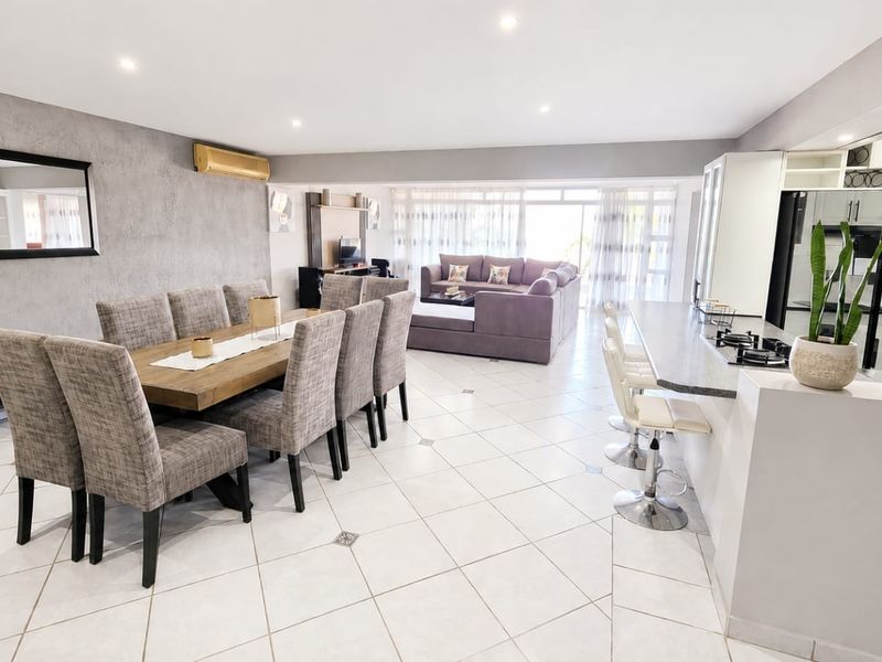 Spacious open-plan living and dining area featuring tiled floors, recessed lighting, and a modern kitchen with a breakfast bar and built-in hob.