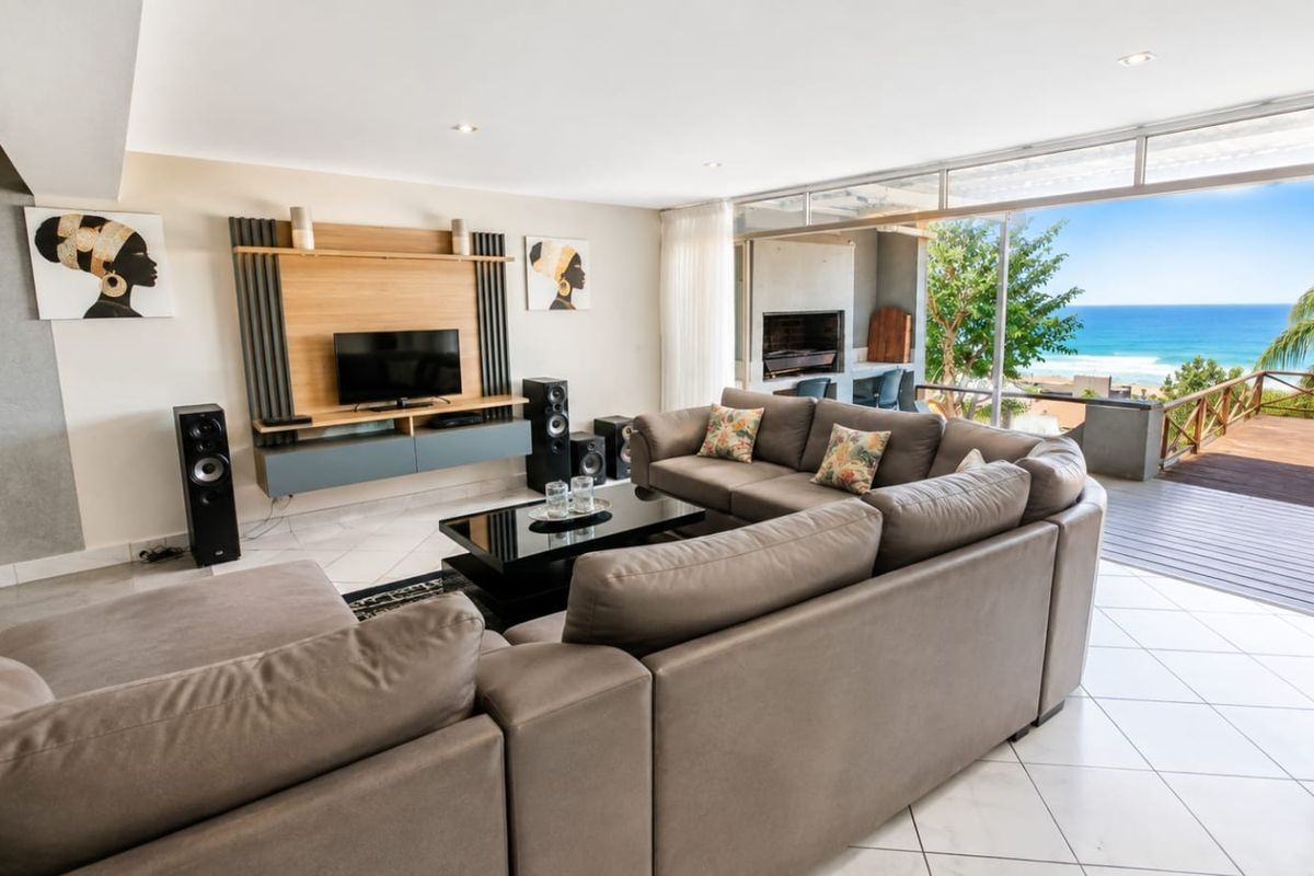Spacious living room featuring tiled floors, a built-in media console, and large sliding doors opening to a deck with ocean views.