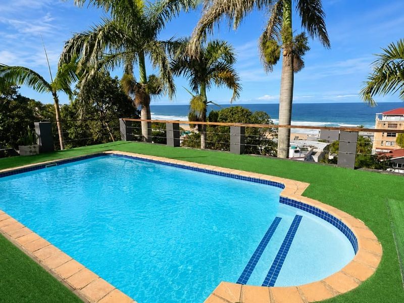 Outdoor swimming pool area featuring artificial turf, cable railing, and panoramic ocean views.