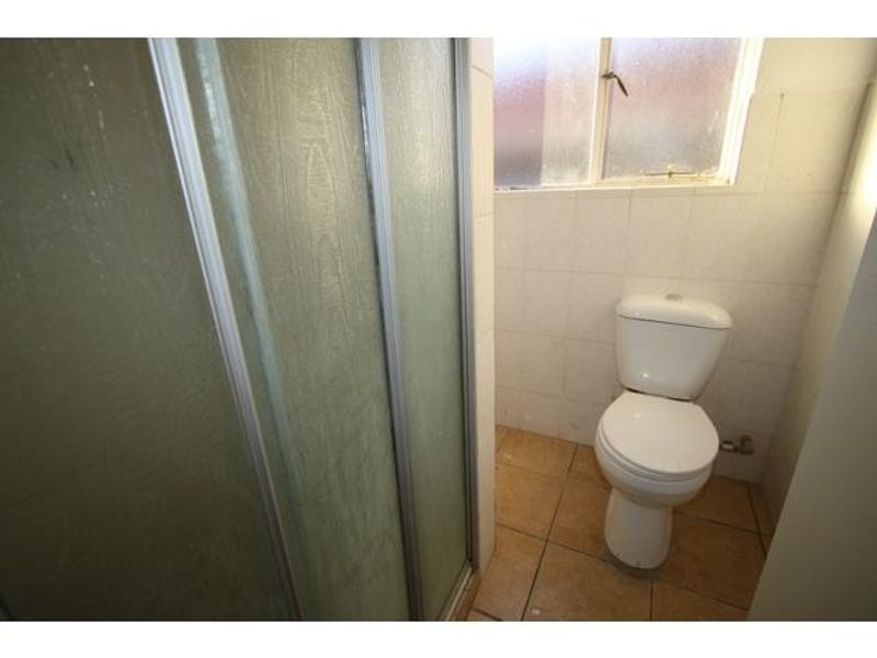 A functional bathroom featuring a shower enclosure, toilet, and tiled finishes, requiring cosmetic updates to improve its overall aesthetic and condition.