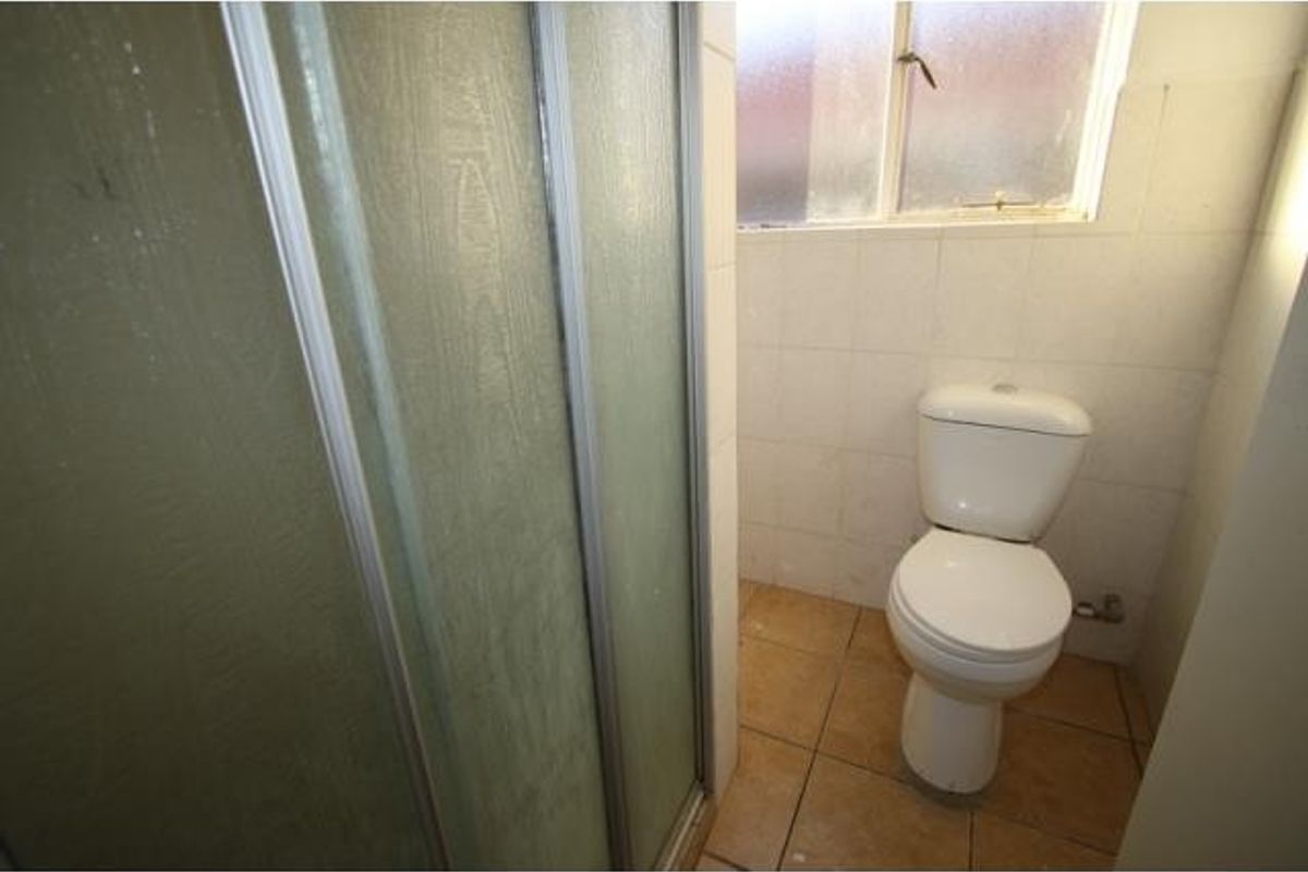 A functional bathroom featuring a shower enclosure, toilet, and tiled finishes, requiring cosmetic updates to improve its overall aesthetic and condition.