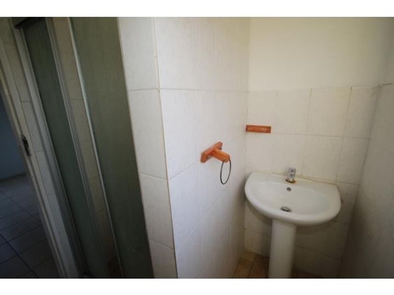 A compact bathroom featuring a pedestal basin, tiled walls, and a shower enclosure, presenting a dated aesthetic in need of modernization.