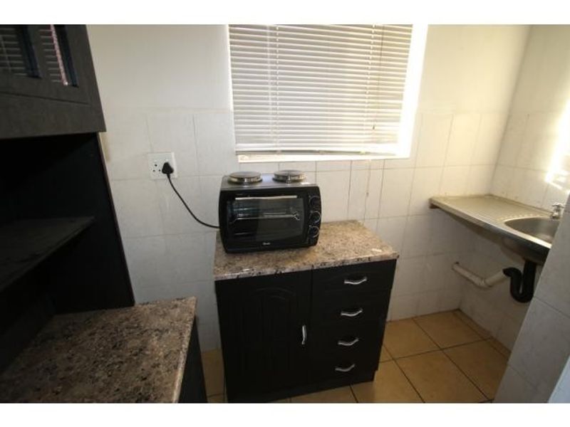 Compact kitchen area featuring dark cabinetry, granite countertops, a stainless steel sink, and tiled finishes, providing a functional space for meal preparation.