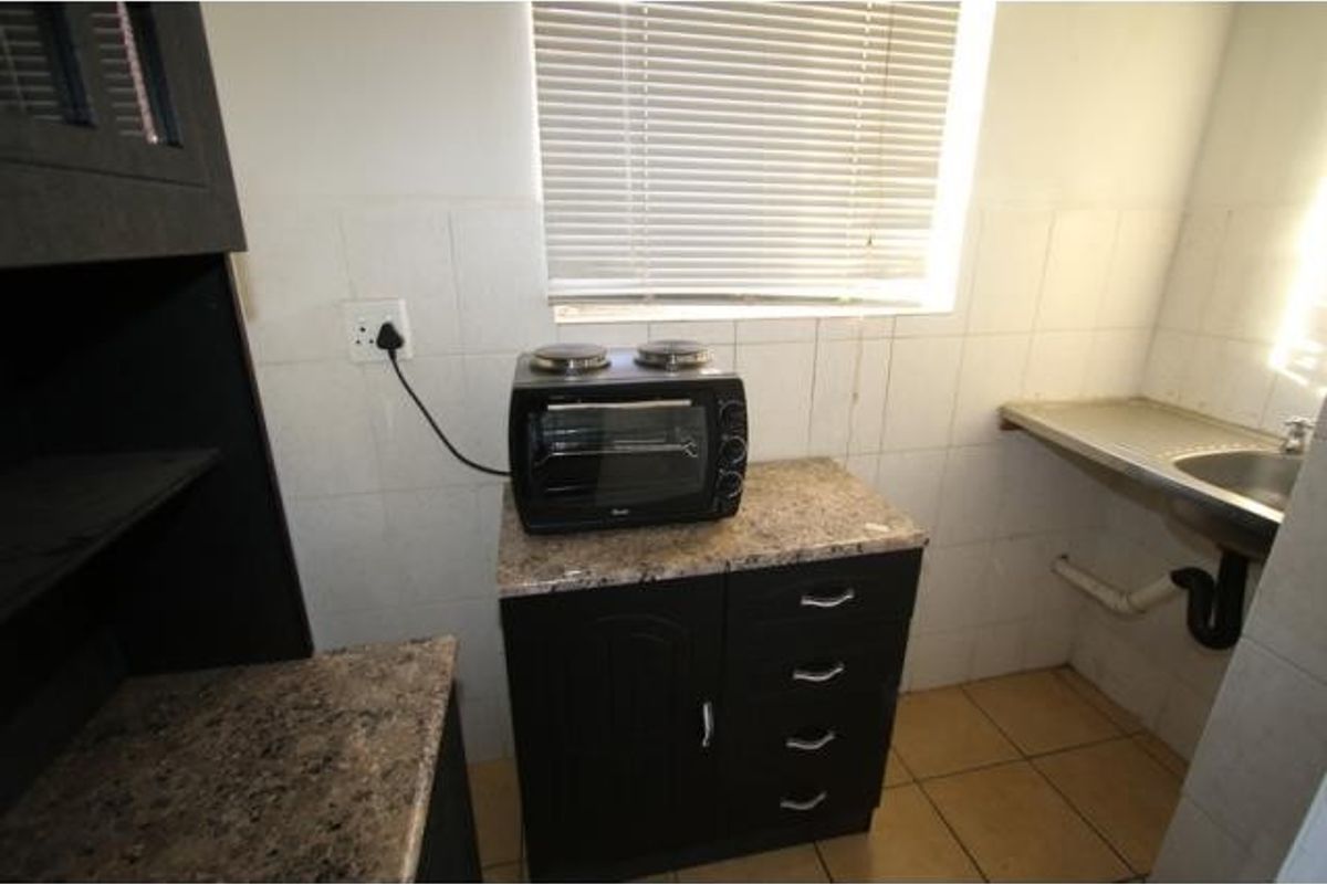 Compact kitchen area featuring dark cabinetry, granite countertops, a stainless steel sink, and tiled finishes, providing a functional space for meal preparation.