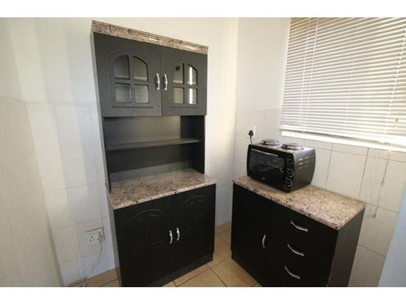 A functional kitchen area featuring dark built-in cabinetry, stone-look laminate countertops, tiled splashbacks, and natural light through venetian blinds.