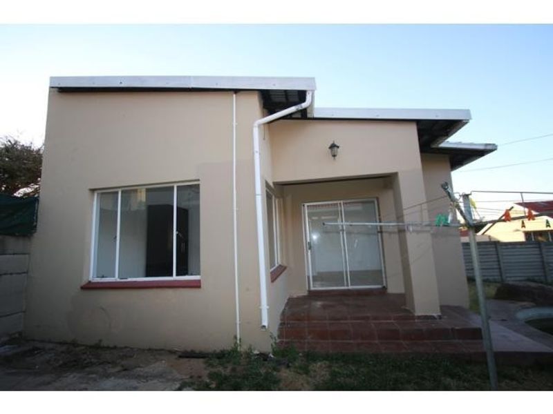 Rear exterior view of the apartment featuring a tiled patio, sliding glass door access, and external wall lighting.