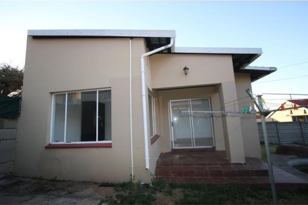 Rear exterior view of the apartment featuring a tiled patio, sliding glass door access, and external wall lighting.