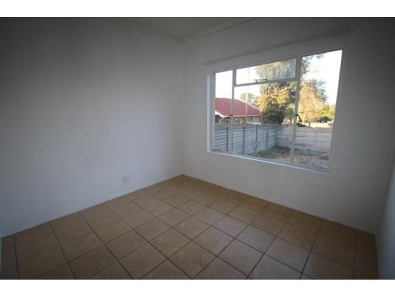 A bright, empty bedroom featuring neutral tiled flooring and a large window providing natural light and a view of the exterior.