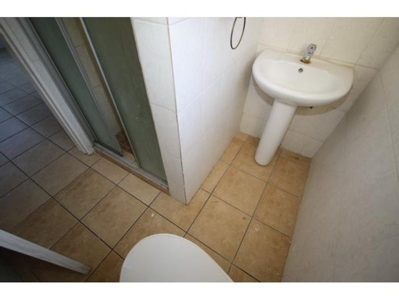 A compact bathroom featuring a pedestal basin, shower enclosure, and tiled finishes, currently in need of cosmetic updates.