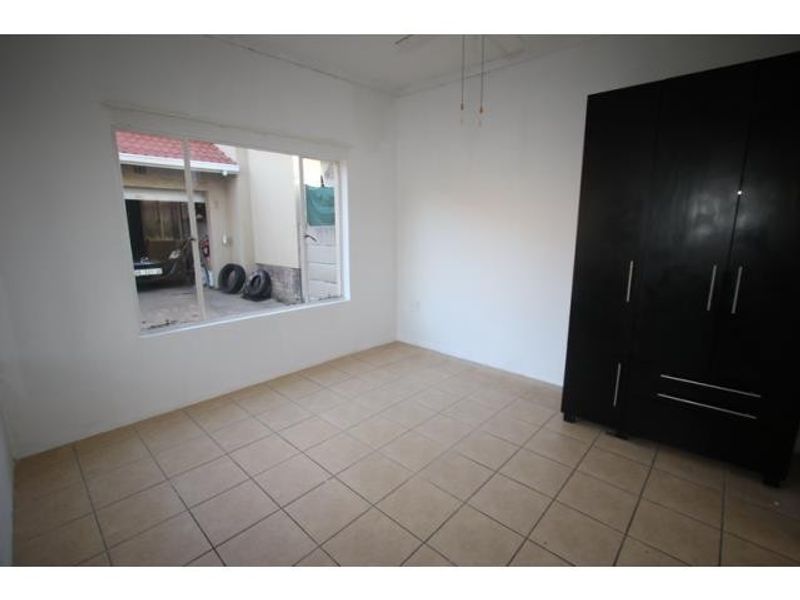 A bright, empty bedroom featuring neutral tiled flooring and a large built-in dark wood wardrobe, offering a clean canvas for personalization.
