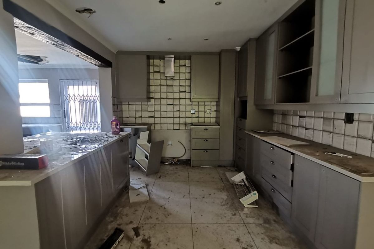 A kitchen in need of significant renovation, featuring built-in cabinetry, stone countertops, and a tiled backsplash, currently in a state of disrepair.
