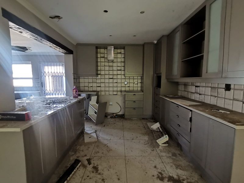 A kitchen in need of significant renovation, featuring built-in cabinetry, stone countertops, and a tiled backsplash, currently in a state of disrepair.