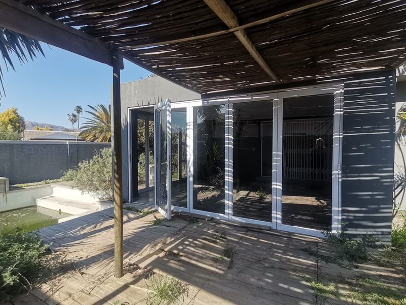 Outdoor patio area featuring timber decking and a pergola, with direct access to the interior through aluminium stacker doors and an adjacent swimming pool.