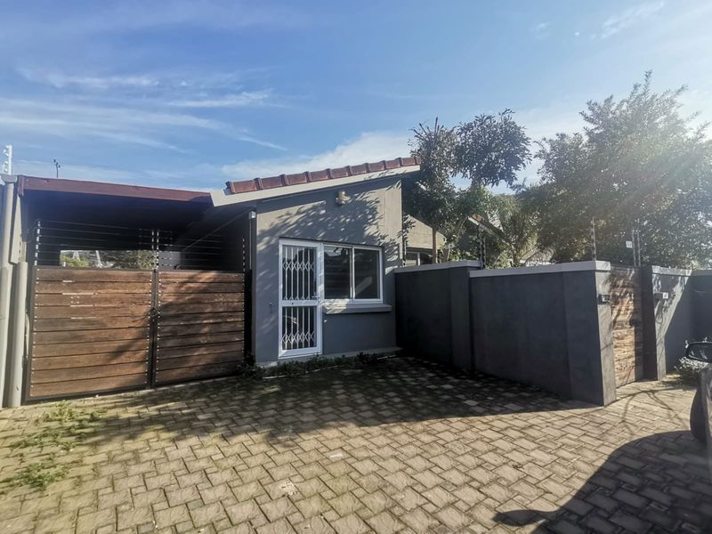 Front exterior view of the property featuring a paved driveway, secure perimeter wall with electric fencing, and a covered carport area.