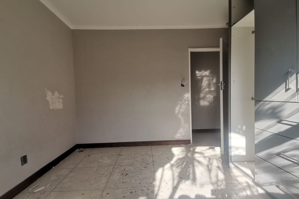 An empty bedroom featuring tiled flooring and built-in cupboards, requiring minor cosmetic repairs and fresh paint to restore its appeal.