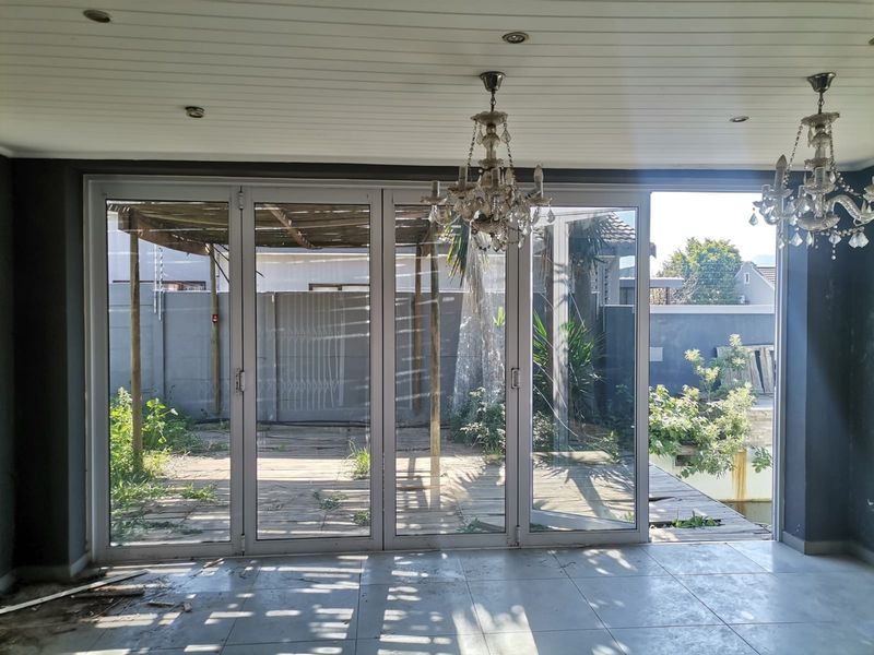 Spacious living area featuring large stacking glass doors that open onto a rear patio and garden, with tiled floors and decorative chandeliers.