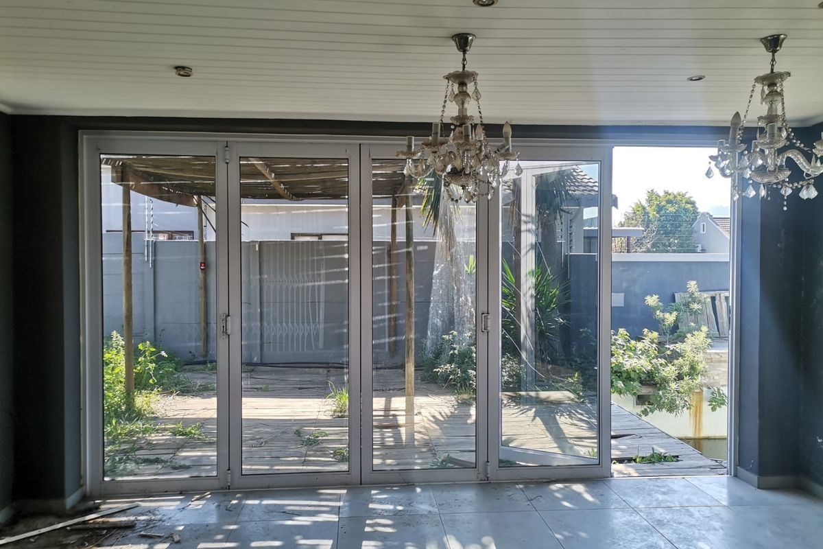 Spacious living area featuring large stacking glass doors that open onto a rear patio and garden, with tiled floors and decorative chandeliers.