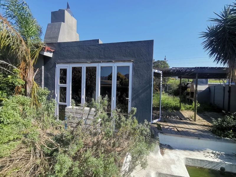 Rear exterior view featuring a dark-painted structure with bi-fold doors, an outdoor fireplace, wooden decking, and a swimming pool in need of maintenance.