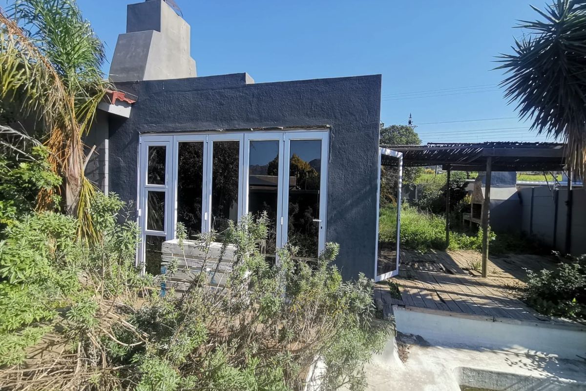 Rear exterior view featuring a dark-painted structure with bi-fold doors, an outdoor fireplace, wooden decking, and a swimming pool in need of maintenance.