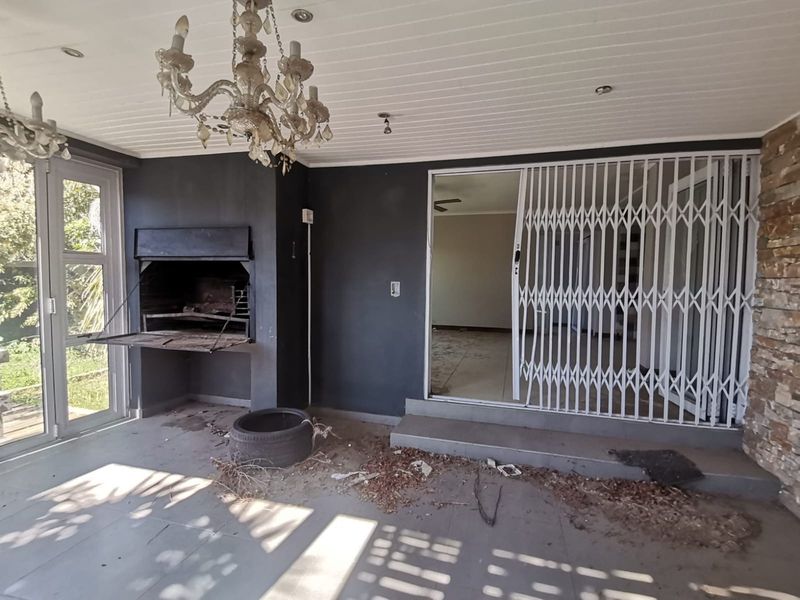 Covered patio area featuring a built-in braai, stone cladding, and sliding security gate access to the interior living space.