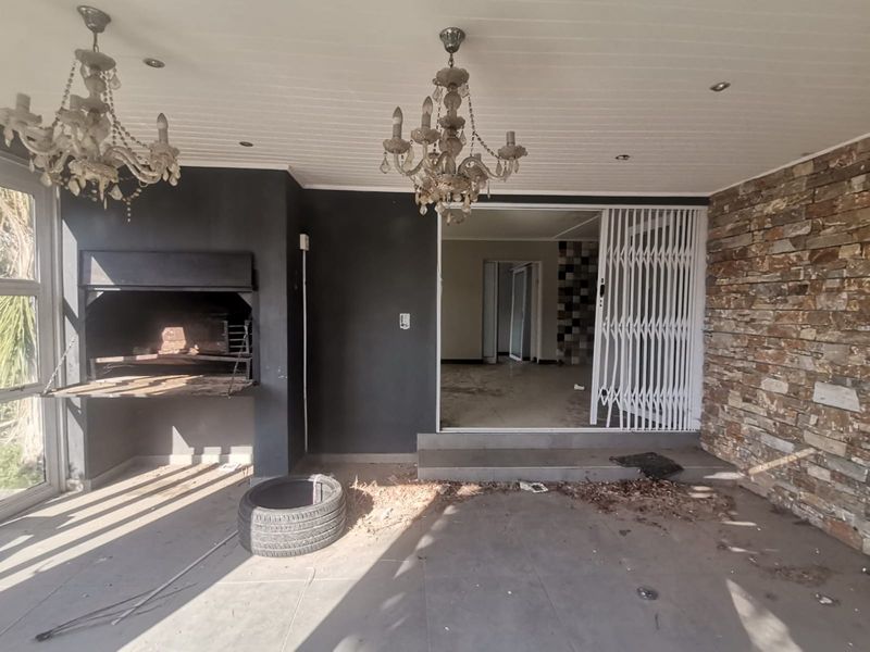 Covered patio area featuring a built-in braai, stone feature wall, and tiled flooring, providing a versatile outdoor entertainment space.