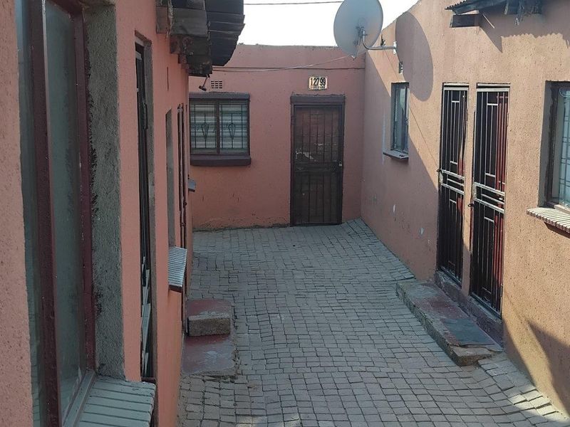 A paved rear courtyard area featuring multiple access points with security gates and burglar bars on windows.
