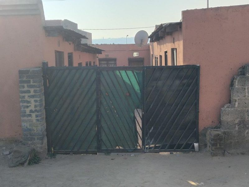 Front exterior view of the property featuring a metal security gate and masonry boundary walls showing signs of wear and weathering.