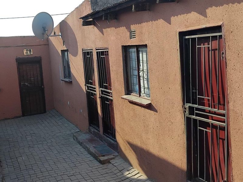 A paved rear courtyard area featuring multiple access points with security gates and burglar bars on windows.