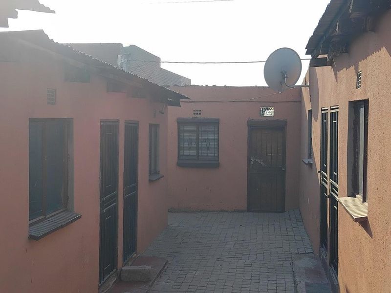 A narrow paved courtyard area between two residential structures, featuring multiple security-gated entrances and a satellite dish installation.