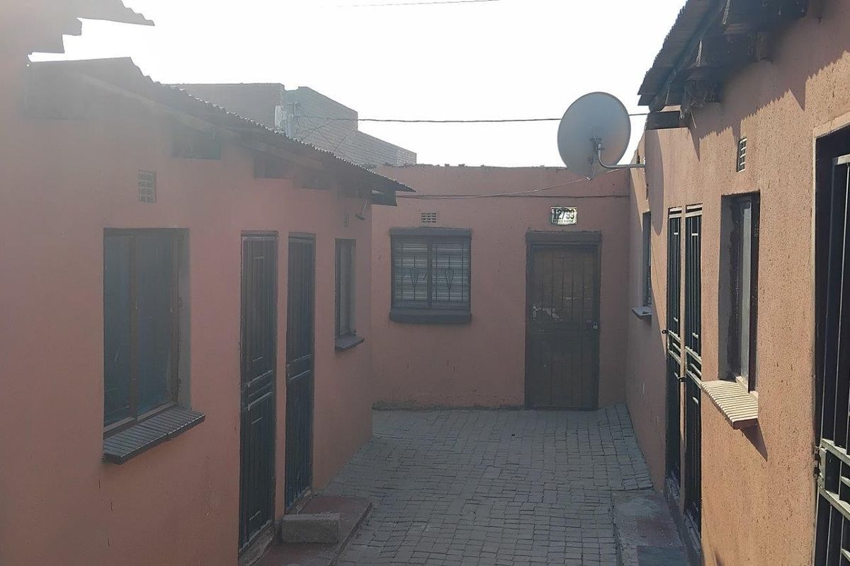 A narrow paved courtyard area between two residential structures, featuring multiple security-gated entrances and a satellite dish installation.