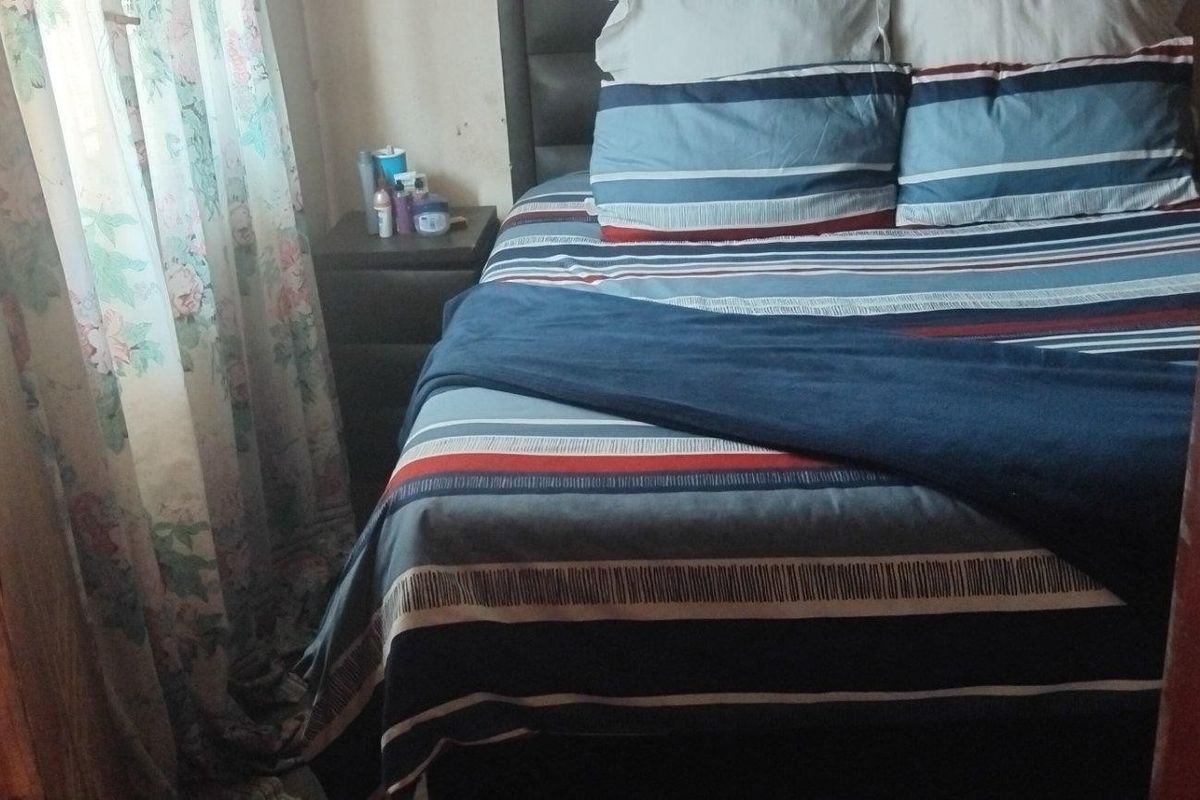 A compact bedroom featuring a double bed, showing signs of wear on the surrounding door frame and wall finishes.