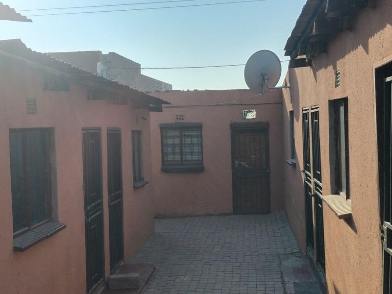 A paved courtyard area between residential units featuring security gates, metal window bars, and a satellite dish installation.