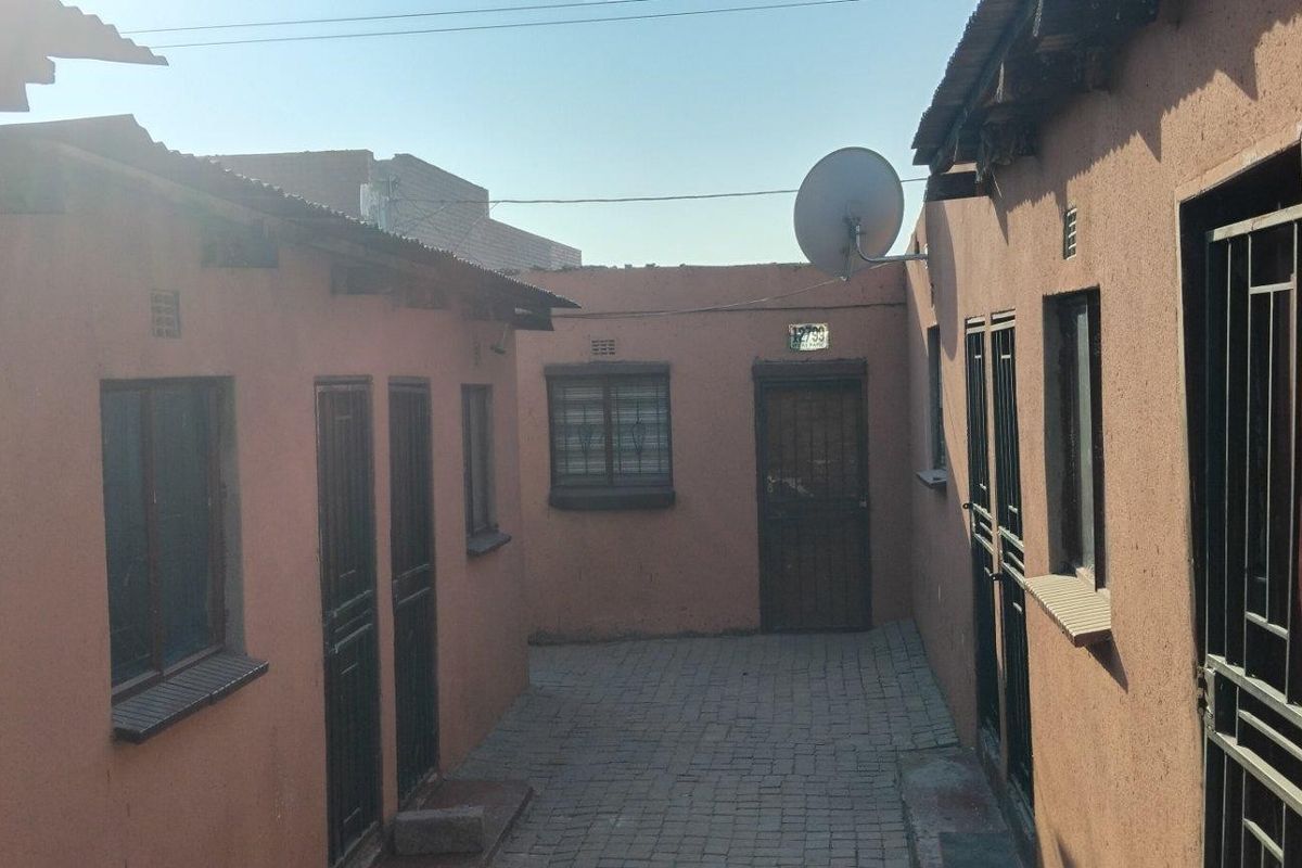 A paved courtyard area between residential units featuring security gates, metal window bars, and a satellite dish installation.