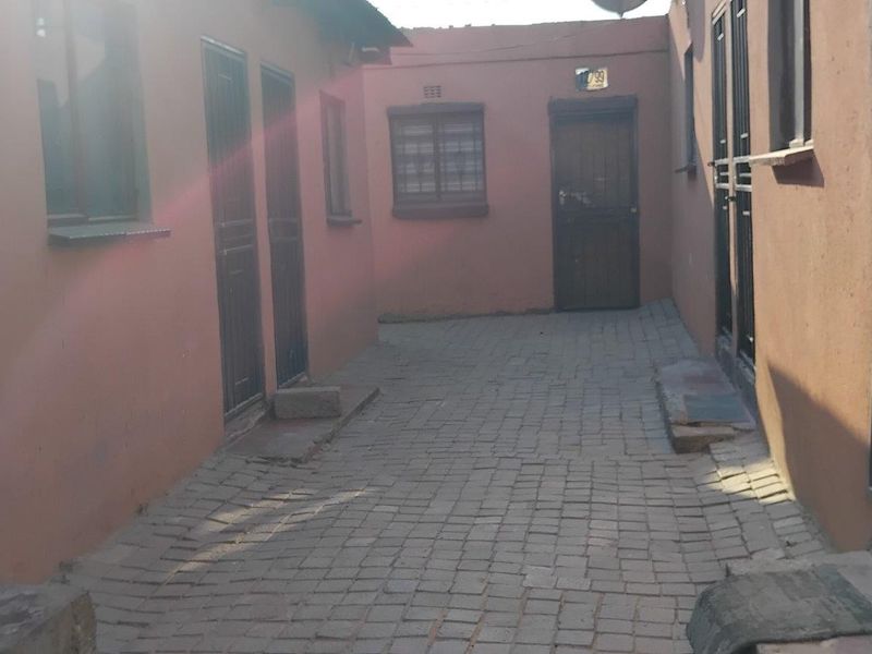 A paved exterior courtyard area providing access to multiple residential units, featuring security gates and bars on all doors and windows.