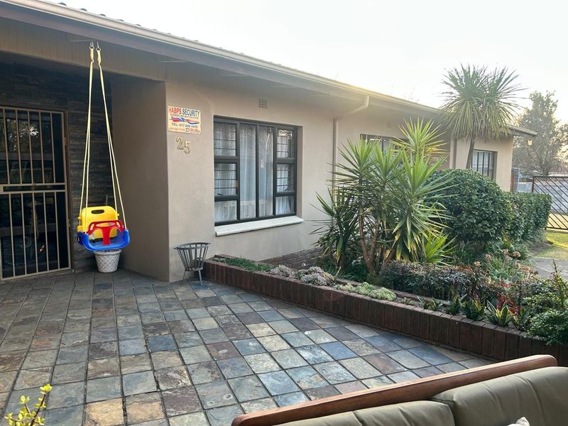 Front entrance area featuring a slate tiled patio, brick planter box, and secure aluminium window frames with security bars.