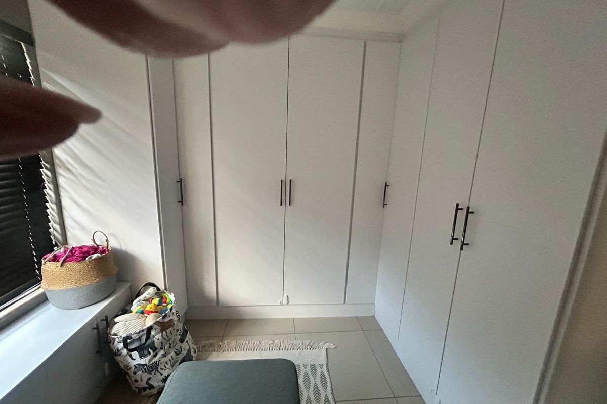 A bedroom featuring white built-in cupboards and tiled flooring, with natural light entering through a window with venetian blinds.